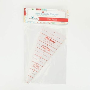 Puede incluir: Un paquete de plástico transparente que contiene una regla para tartas blanca y roja. La regla tiene forma de triángulo y tiene marcas rojas para medir. El texto en la regla dice "Pie Ruler" y "Cut 16 Slices to make 1 Pie!". El paquete también tiene el texto "Sew Simple Shapes" y "Riley Blake".