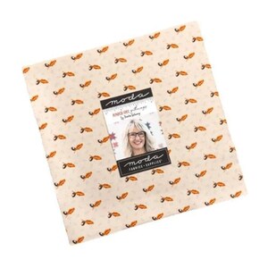 Pode incluir: Um pacote de tecido quadrado com fundo creme e um padrão repetido de folhas laranja. Uma etiqueta com o logotipo da Moda e um retrato de uma mulher está anexada. O tecido é provavelmente para projetos de quilting ou costura.