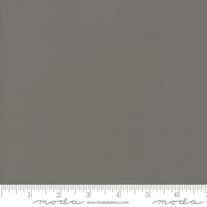 May include: A solid gray fabric with a subtle texture. The fabric is a neutral color, suitable for various sewing and crafting projects. The image includes a ruler along the bottom edge, with the brand name "moda" visible.