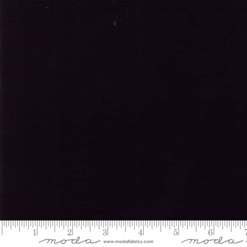 May include: A solid black fabric swatch with a ruler showing measurements in inches. The ruler has the word "moda" printed on it.