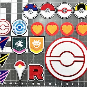 May include: A collection of embroidered iron-on patches featuring various Pokemon characters and symbols. The patches are in a variety of colors, including red, blue, yellow, green, and white. The patches are arranged in a grid pattern on a white background.
