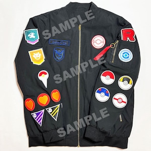 May include: Black bomber jacket with multiple colorful embroidered patches. Patches include various shapes, logos, and the text "Joshua Chris". The jacket has a zipper closure, a red pull tab, and ribbed cuffs and hem.
