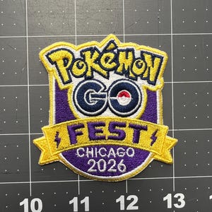 May include: Embroidered patch featuring the Pokémon GO Fest Chicago 2026 logo. The patch has a yellow border with the words "Pokémon GO" in yellow and the word "FEST" in purple. The patch is approximately 3 inches wide.