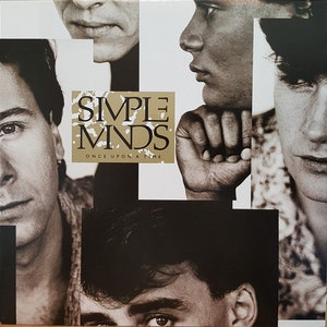 Peut inclure: Une pochette d'album vinyle avec un collage de photos en noir et blanc de quatre visages d'hommes. Le titre de l'album "SIMPLE MINDS" et le sous-titre de l'album "ONCE UPON A TIME" sont imprimés en lettres dorées sur fond blanc.