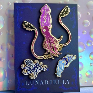 May include: A set of four enamel pins featuring a purple squid, a blue squid, and two different blue and white octopus designs. The pins are on a black card with the text "LUNARJELLY".
