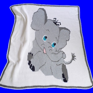 May include: A white crocheted baby blanket with a gray elephant design. The elephant has blue eyes and a pink tongue.