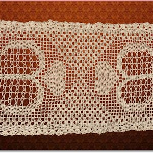 May include: A white crocheted table runner with a delicate pattern. The runner features a repeating design of small, open circles.