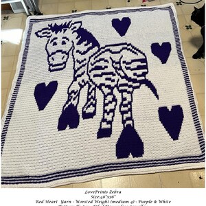 Pode incluir: Uma manta de crochê com uma zebra roxa e branca com corações. A manta mede 122 cm por 142 cm e é feita com fio de peso médio.