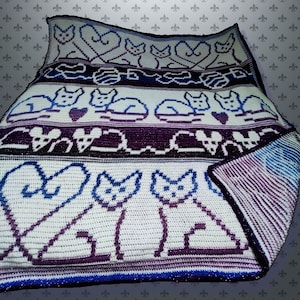 May include: A crocheted blanket featuring a repeating pattern of cats and hearts in shades of blue, purple, and white. The blanket has a textured appearance and a decorative border. The design includes stylized cat silhouettes and heart shapes.