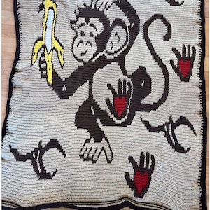 Könnte beinhalten: Eine gehäkelte Decke mit einem Affen, der eine Banane hält, mit Herzen und Händen im Hintergrund. Die Decke ist aus braunem, beigefarbenem, rotem und gelbem Garn gefertigt. Der Text "LovePrints Monkey Blanket Pattern Overlay Mosaic Crochet I Love this Yarn 5mm hook. Pattern Tester Jen Scott" befindet sich am unteren Rand des Bildes.