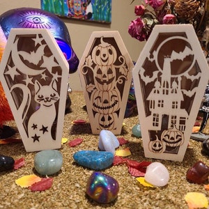 Peut inclure: Trois cercueils lumineux en bois sur le th&egrave;me d'Halloween. Le premier cercueil repr&eacute;sente un chat et des &eacute;toiles, le second une pile de citrouilles, et le troisi&egrave;me une maison hant&eacute;e et des citrouilles.