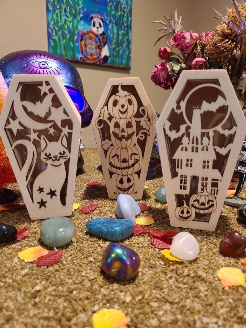 Peut inclure: Trois cercueils lumineux en bois sur le th&egrave;me d'Halloween. Le premier cercueil repr&eacute;sente un chat et des &eacute;toiles, le second une pile de citrouilles, et le troisi&egrave;me une maison hant&eacute;e et des citrouilles.