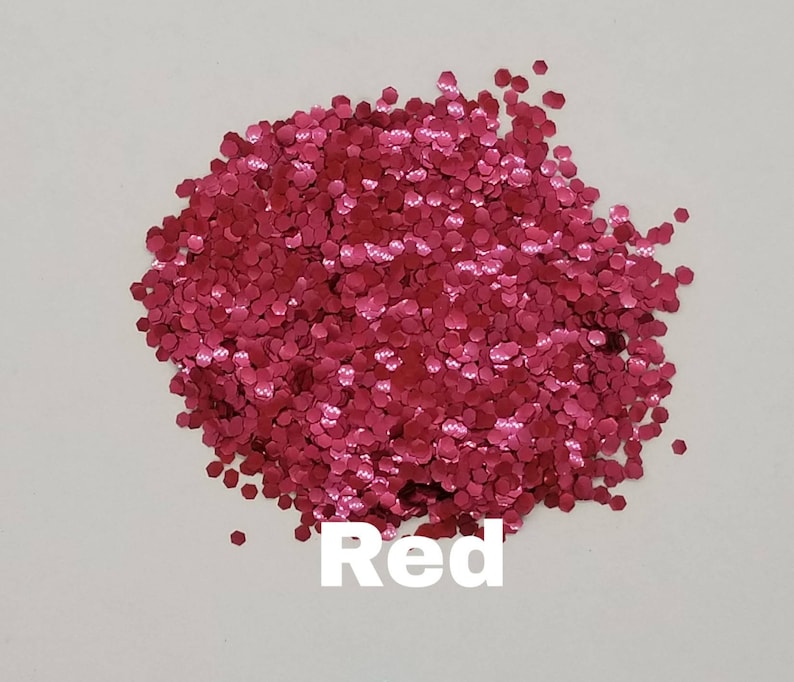 May include: A pile of red glitter, with a hexagonal shape. The glitter is on a white background. The word "Red" is written below the glitter.