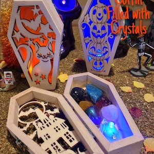Peut inclure: Trois bo&icirc;tes en bois en forme de cercueil sur le th&egrave;me d'Halloween. La premi&egrave;re bo&icirc;te a un motif de chat et de lune, la deuxi&egrave;me a une pile de citrouilles, et la troisi&egrave;me est ouverte pour r&eacute;v&eacute;ler une collection de cristaux. Le texte "Halloween Coffin Filled with Crystals" est &eacute;crit sur l'image.