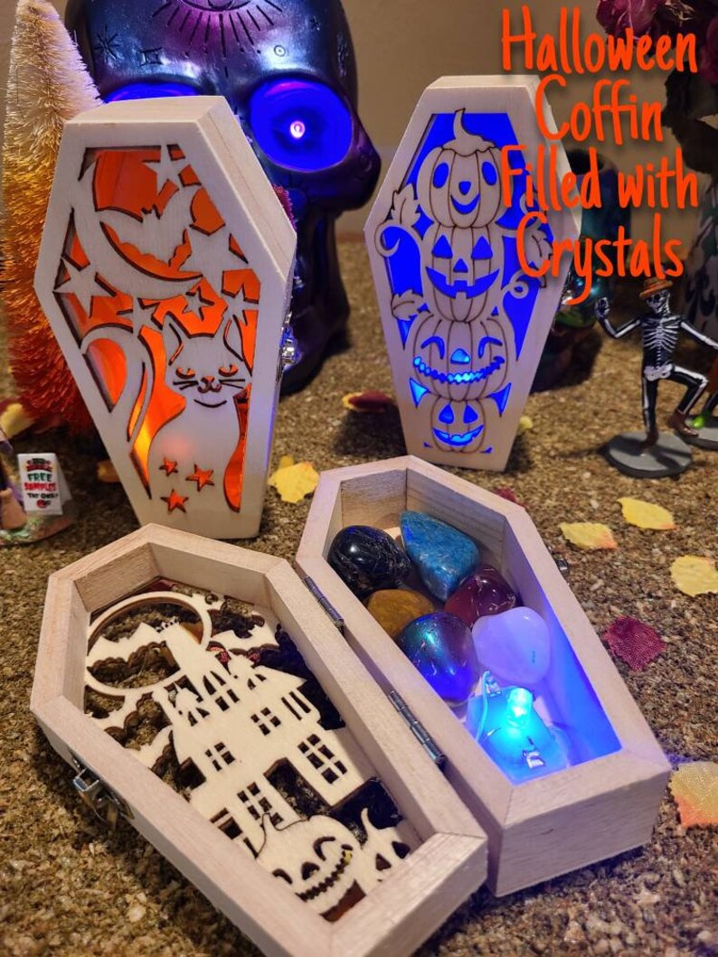 Peut inclure: Trois bo&icirc;tes en bois en forme de cercueil sur le th&egrave;me d'Halloween. La premi&egrave;re bo&icirc;te a un motif de chat et de lune, la deuxi&egrave;me a une pile de citrouilles, et la troisi&egrave;me est ouverte pour r&eacute;v&eacute;ler une collection de cristaux. Le texte "Halloween Coffin Filled with Crystals" est &eacute;crit sur l'image.