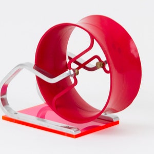 May include: A red, 3D printed, spinning wheel with a silver metal stand. The wheel is mounted on a clear acrylic base with a pink and orange design.