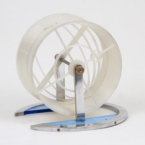 May include: A clear, cylindrical wheel with an internal lattice structure, mounted on a silver-colored metal frame with blue accents. The wheel is supported by two vertical metal supports and a curved base.