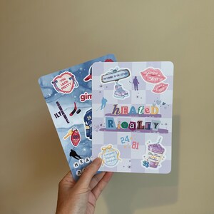May include: Two rectangular sticker sheets featuring various designs. One sheet has a blue marble background with hockey-themed stickers, including a heart with text 'YOU LOOK PRETTY'. The other sheet has a light purple checkerboard pattern with text 'HEATED RIVALRY', ice skates, lips, and a 'Blue Moon Brooklyn' drink graphic.