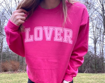 May include: A pink sweatshirt with the word "LOVER" printed in white on the front.