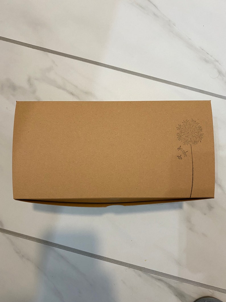 May include: A brown cardboard box with a simple design of a dandelion on the top right corner.