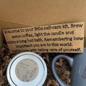May include: A self-care kit with a gray mug, a small tin of shea and coconut body butter, and a note that reads "Welcome to your little self-care kit. Brew some coffee, light the candle and enjoy a long hot bath. Remembering how important you are to this world. Fall in love with taking care of yourself."