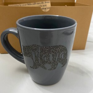 May include: A gray ceramic mug with a black glitter bear silhouette and the word "Mama" inside the bear.