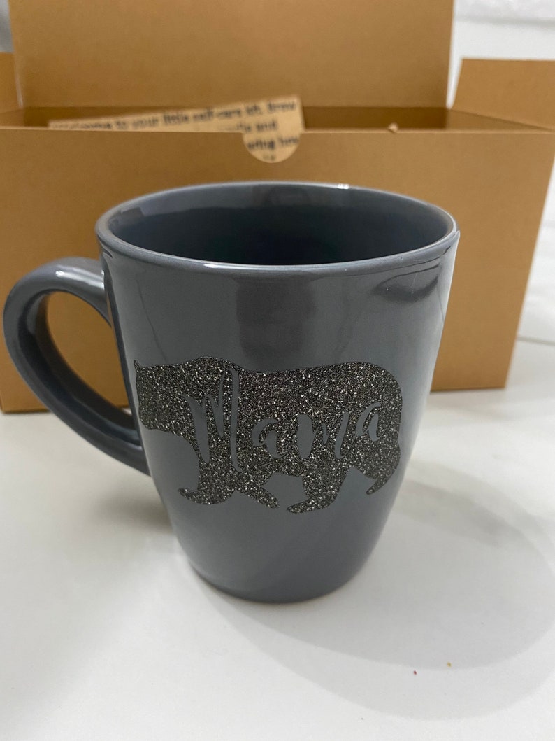 May include: A gray ceramic mug with a black glitter bear silhouette and the word "Mama" inside the bear.