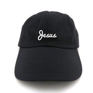 May include: Black baseball cap with a curved brim. The word "Jesus" is embroidered in white script on the front of the cap. The cap is made of a soft fabric and has an adjustable strap.
