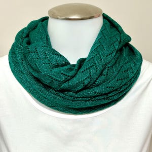 May include: A vibrant emerald green infinity scarf with a delicate openwork pattern. The scarf is draped around a mannequin's neck, showcasing its texture and design. The scarf is made of a soft, lightweight material.