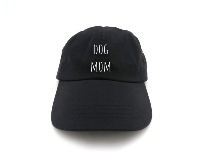 May include: Black baseball cap with the words "DOG MOM" in white block letters. The cap has a curved brim and a fabric strap in the back for adjustment. The hat is made of a soft, durable material.