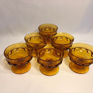May include: Six amber glass dessert dishes with a scalloped rim and a textured base. The dishes are arranged in a circle on a white surface.
