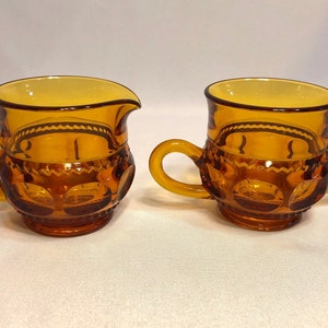 May include: A set of two amber glass creamer and sugar bowls with a textured design. The bowls have two handles and a rounded shape.