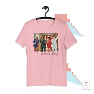May include: Pink t-shirt with a graphic of four people in pajamas standing in a hallway. The text "your friends copied us." is printed below the graphic.