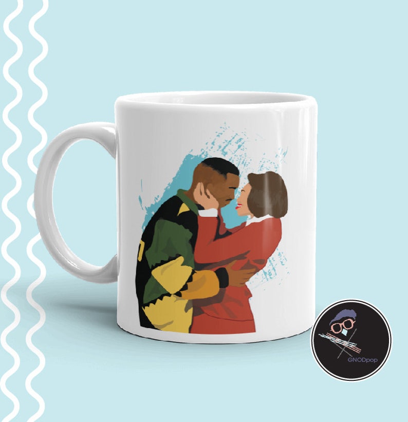 Puede incluir: Taza de cer&aacute;mica blanca con una ilustraci&oacute;n colorida de una pareja abraz&aacute;ndose. El hombre lleva una chaqueta verde y amarilla y la mujer lleva un vestido rojo. El fondo es un dise&ntilde;o abstracto azul y blanco.