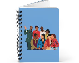 May include: A blue spiral notebook with a colorful illustration of a group of people. The people are all wearing different clothes and have different hairstyles. The illustration is in a cartoon style.