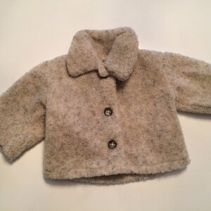 May include: A cream-colored baby jacket with a fuzzy texture and three buttons.