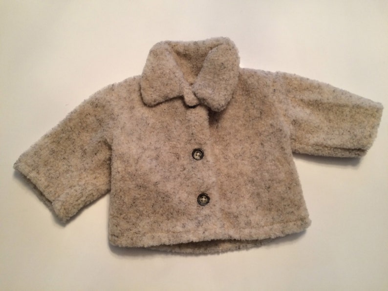 May include: A cream-colored baby jacket with a fuzzy texture and three buttons.