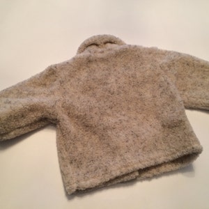 May include: A cream-colored, fuzzy jacket with a slightly textured surface. The jacket has long sleeves and a button closure.