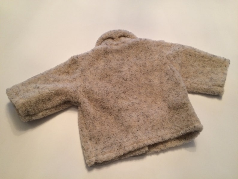 May include: A cream-colored, fuzzy jacket with a slightly textured surface. The jacket has long sleeves and a button closure.