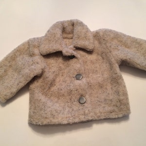May include: A cream-colored, fuzzy jacket with a button closure. The jacket has a collar and long sleeves.