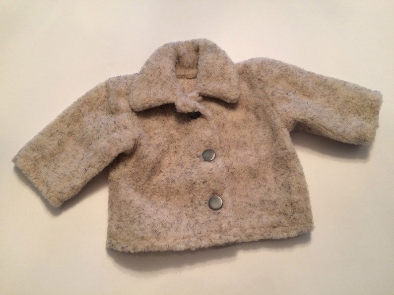 May include: A cream-colored, fuzzy jacket with a button closure. The jacket has a collar and long sleeves.