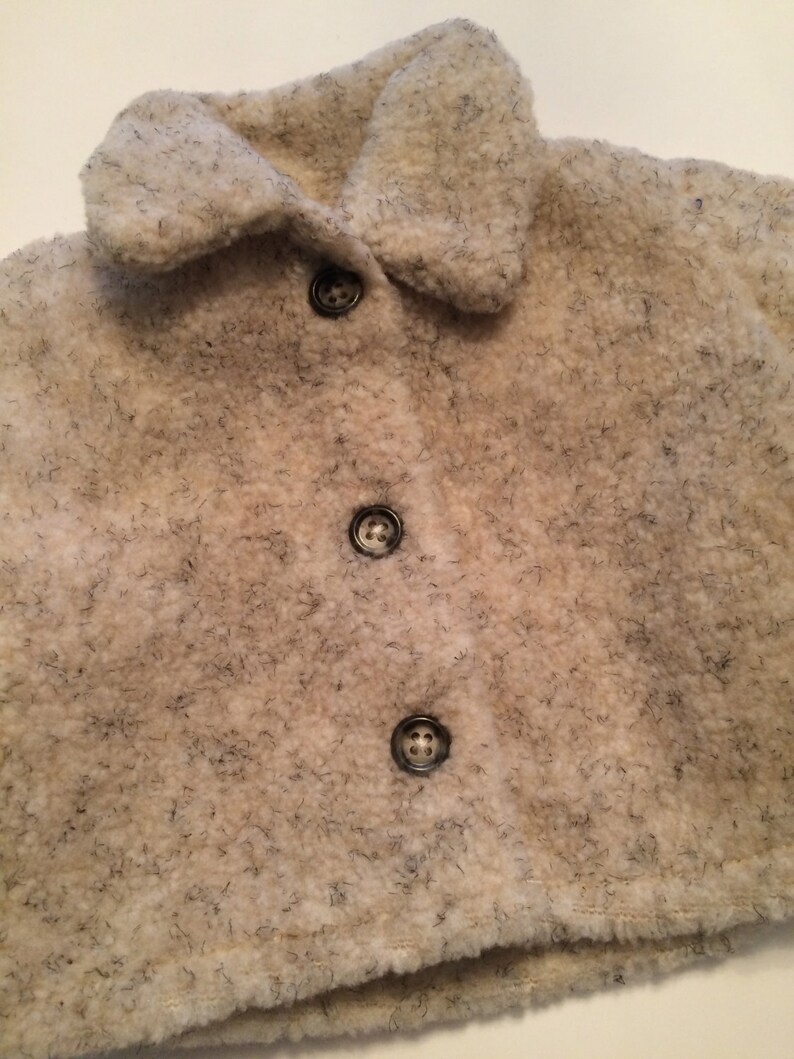 May include: A white, fluffy, faux fur jacket with a collar and four black buttons.