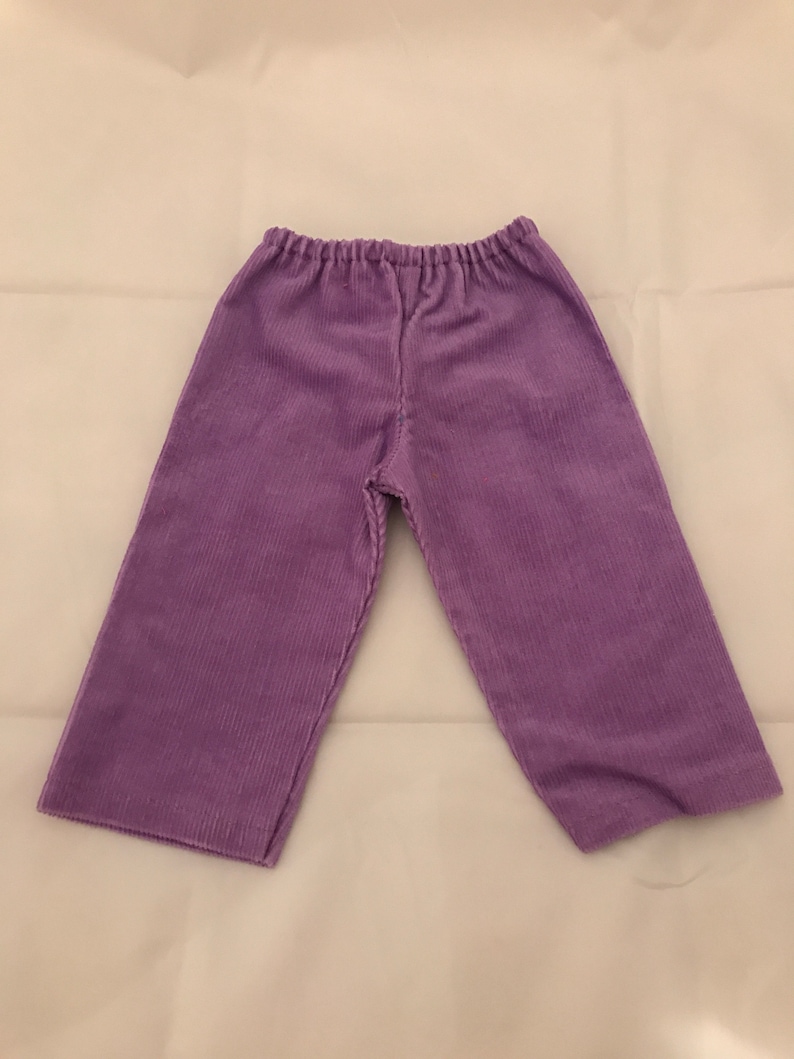 May include: Purple corduroy trousers with a wide leg and elastic waistband.