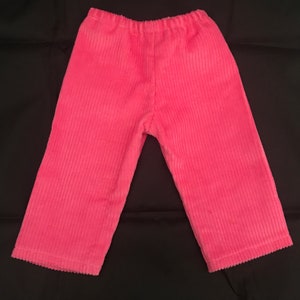 May include: Pink corduroy trousers with a wide leg and elastic waistband.