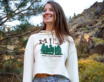 May include: A white cropped hoodie with a green and brown graphic of trees and the text "man, I love forests".
