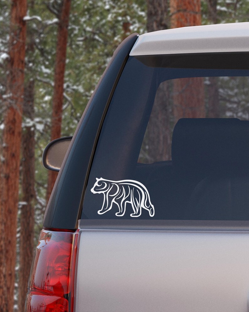 May include: White vinyl decal of a stylized bear silhouette on a silver car window.