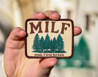 May include: A beige patch with brown stitching and the text "MILF" in brown letters. Below the text are five green trees and the text "man, i love forests".