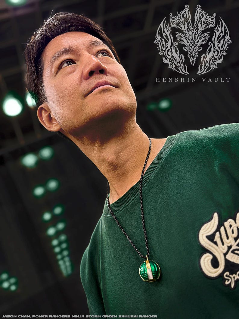 May include: A man wearing a green sweatshirt with a black necklace and a green and gold pendant. The pendant is a sphere with a design that resembles a Power Rangers Ninja Storm Green Samurai Ranger. The text "HENSHIN VAULT" is visible in the upper right corner of the image.