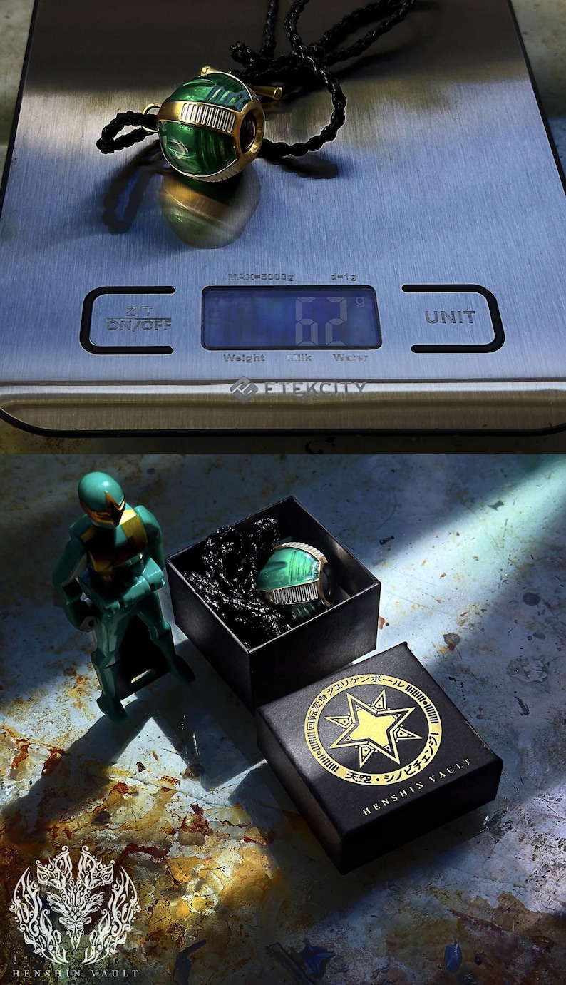 May include: A green and gold metal pendant shaped like a sphere with a black cord. The pendant is on a digital scale that reads 6.2 grams. The pendant is also in a black box with a gold star and Japanese text.
