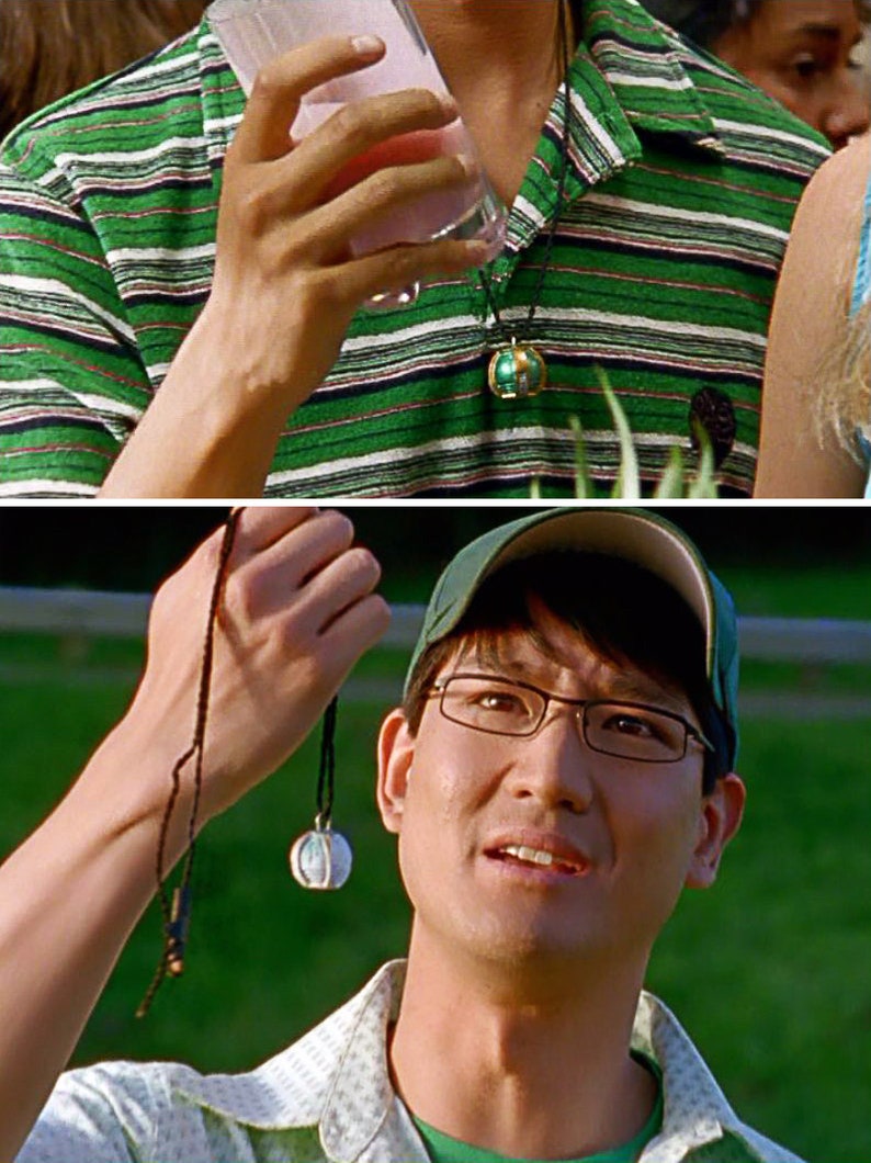 May include: A man wearing a green and white striped shirt with a black necklace and a green globe pendant. He is holding a glass of pink liquid. In the second image, the man is wearing a green baseball cap and glasses. He is holding a black necklace with a white globe pendant.